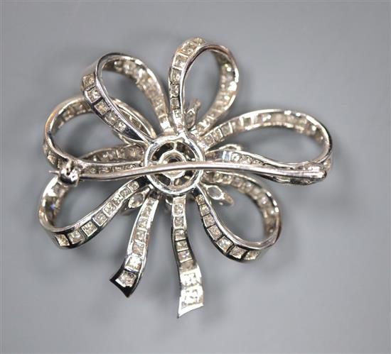 A mid 20th century white metal and diamond cluster set ribbon scroll brooch, 36mm, gross 15.6 grams.